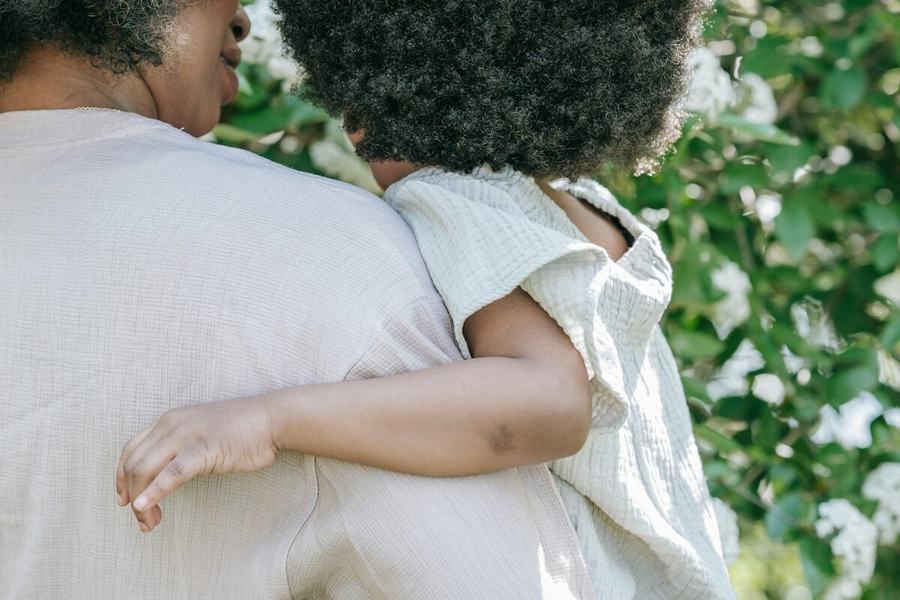 A parent carrying a young child outdoors among greenery